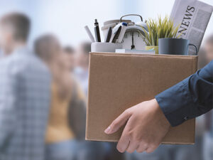 Person carrying box filled with desk items after losing their job.